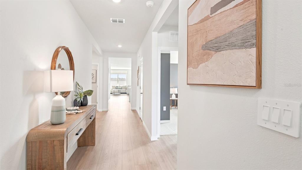 A bright hallway features light wood flooring, a console table with a lamp, and wall art — 1216 ALPINE ASH PLACE SE, RUSKIN, FL