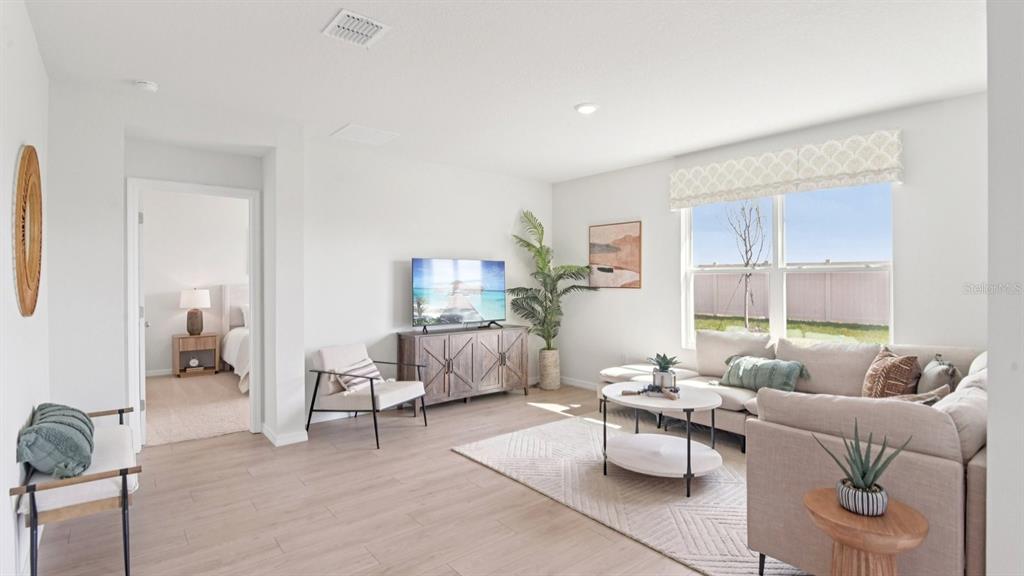 A bright living room features light wood-look flooring, a sectional sofa, and a television console — 1216 ALPINE ASH PLACE SE, RUSKIN, FL