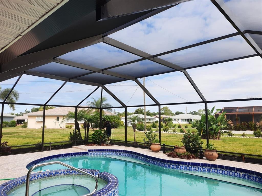 A screened-in pool enclosure with a spa overlooks a grassy backyard and neighboring houses — 910 CAPLES STREET, ENGLEWOOD, FL
