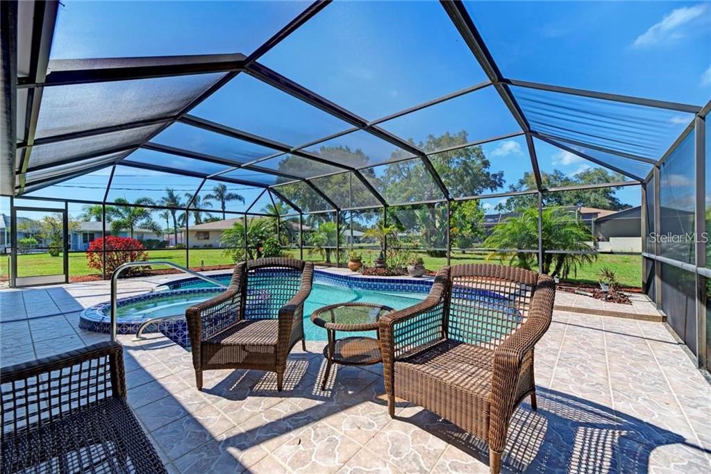 A screened-in pool patio features wicker furniture on a tiled deck overlooking a grassy yard — 910 CAPLES STREET, ENGLEWOOD, FL