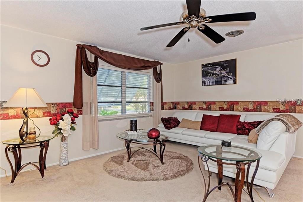 A living room features a white sofa, glass-topped tables, a ceiling fan, and patterned wallpaper — 910 CAPLES STREET, ENGLEWOOD, FL