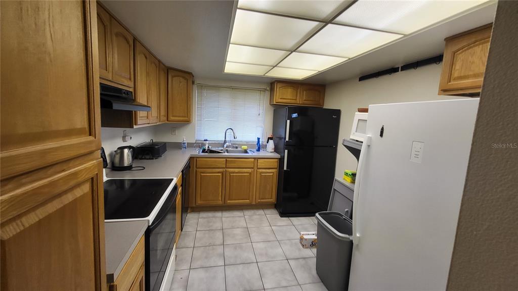 A kitchen features oak cabinets, light countertops, tile flooring, and a mix of appliance colors — 875 S VILLAGE DRIVE N UNIT 102, ST PETERSBURG, FL