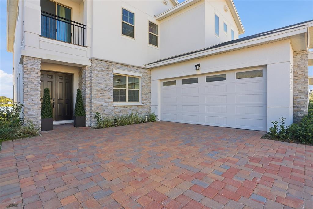 A two-story house exterior features a stone facade, a white garage, and a paver driveway — 5170 BUTTONSAGE, ST CLOUD, FL