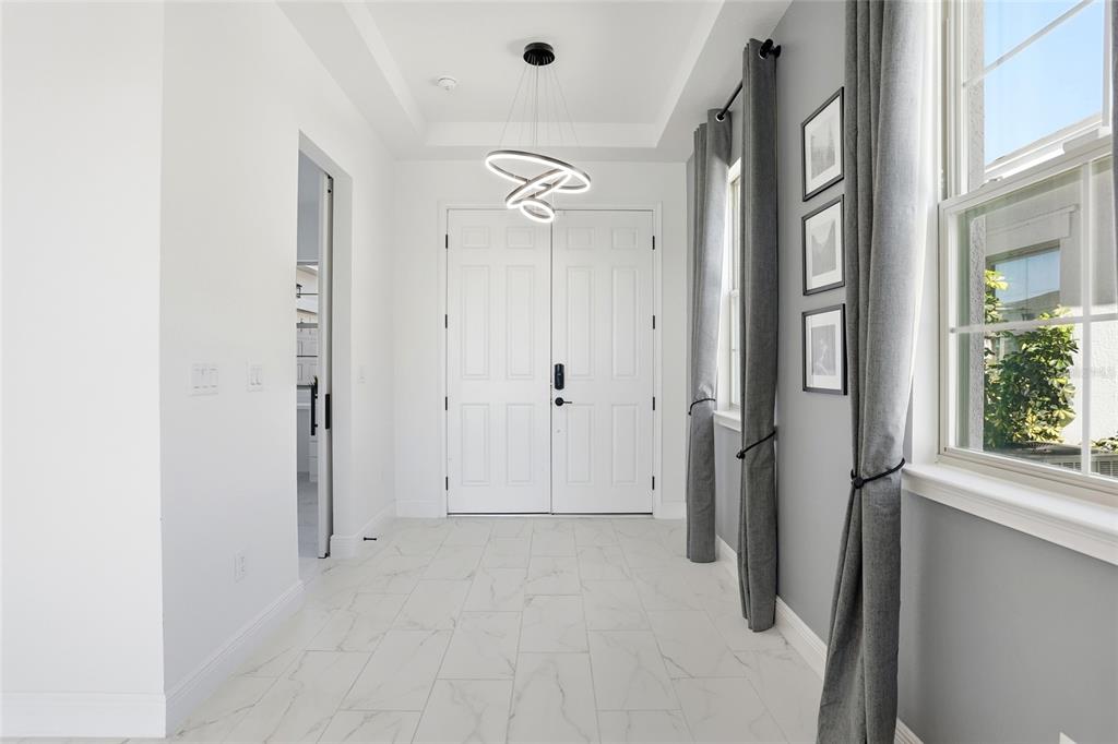 A bright entryway features white tile flooring, a modern chandelier, and gray walls with curtains — 5170 BUTTONSAGE, ST CLOUD, FL