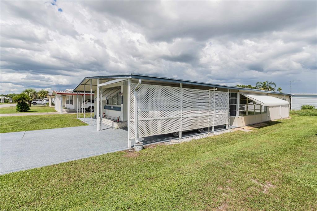 A mobile home with a carport, white lattice skirting, and a metal awning under cloudy skies — 5302 POWHATTAN STREET, ZEPHYRHILLS, FL