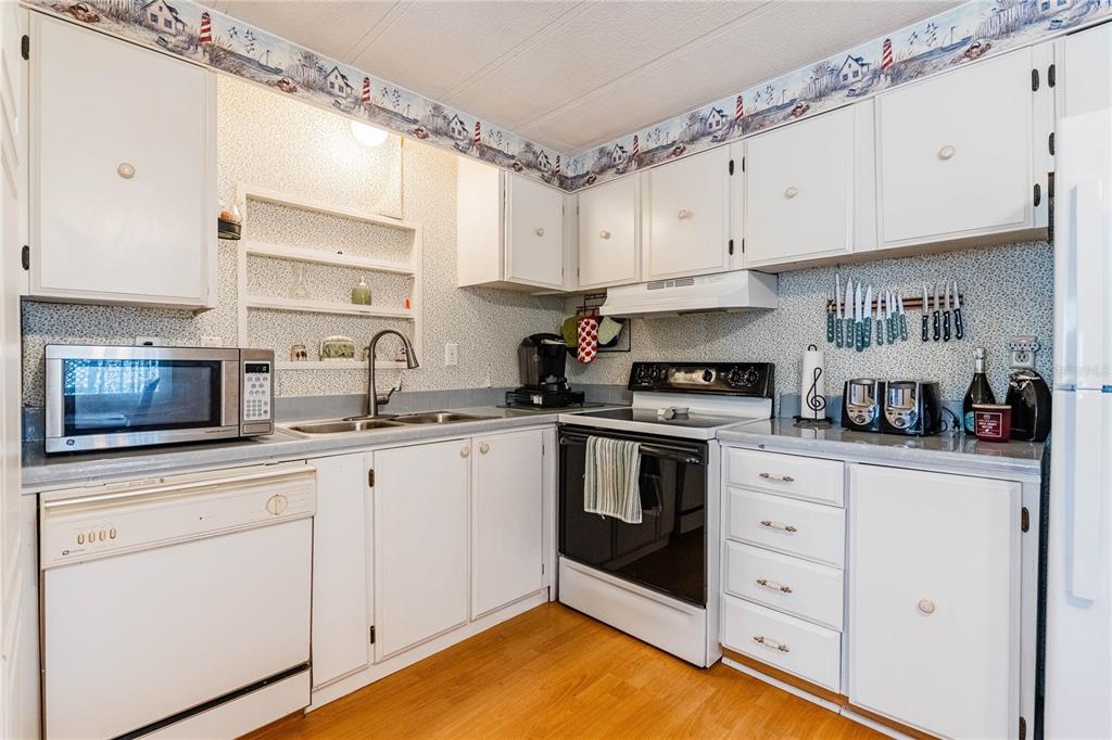 A kitchen with white cabinets, laminate countertops, a microwave, a stove, and nautical-themed wallpaper — 5302 POWHATTAN STREET, ZEPHYRHILLS, FL