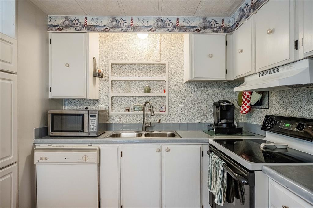 A kitchen features white cabinets, a double sink, a microwave, and patterned wallpaper — 5302 POWHATTAN STREET, ZEPHYRHILLS, FL