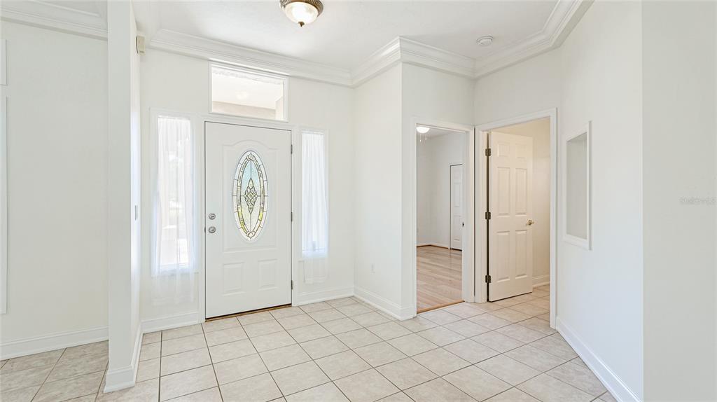 A bright entryway features white walls, tiled flooring, a front door with glass, and crown molding — 534 OAK BAY DRIVE, OSPREY, FL