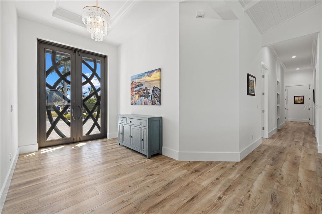 A bright entryway features light wood flooring, a crystal chandelier, and double doors with decorative grilles — 1831 RIO VISTA TERRACE, PARRISH, FL