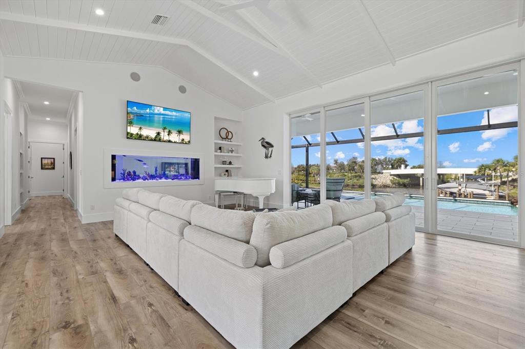 A white living room features a built-in aquarium, a grand piano, and large sliding glass doors — 1831 RIO VISTA TERRACE, PARRISH, FL