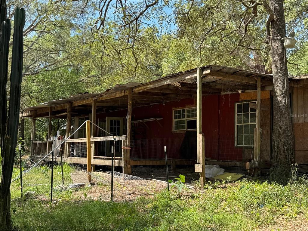 A weathered, red-sided mobile home features a large, rustic wooden porch under a metal roof — 16137 SE 34TH PLACE, OCKLAWAHA, FL