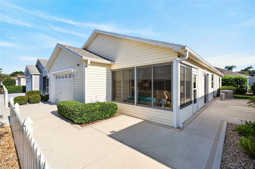 A light-colored house with a garage, screened-in porch, and concrete driveway under a blue sky — 2207 JETTA WAY, THE VILLAGES, FL