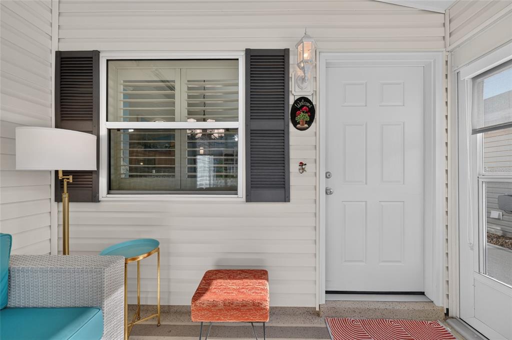 A covered porch features a white door, a window with shutters, and casual outdoor furniture — 2207 JETTA WAY, THE VILLAGES, FL
