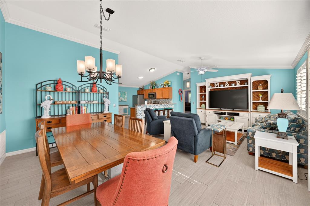 An open-concept living and dining area features light blue walls, wood furniture, and tile flooring — 2207 JETTA WAY, THE VILLAGES, FL