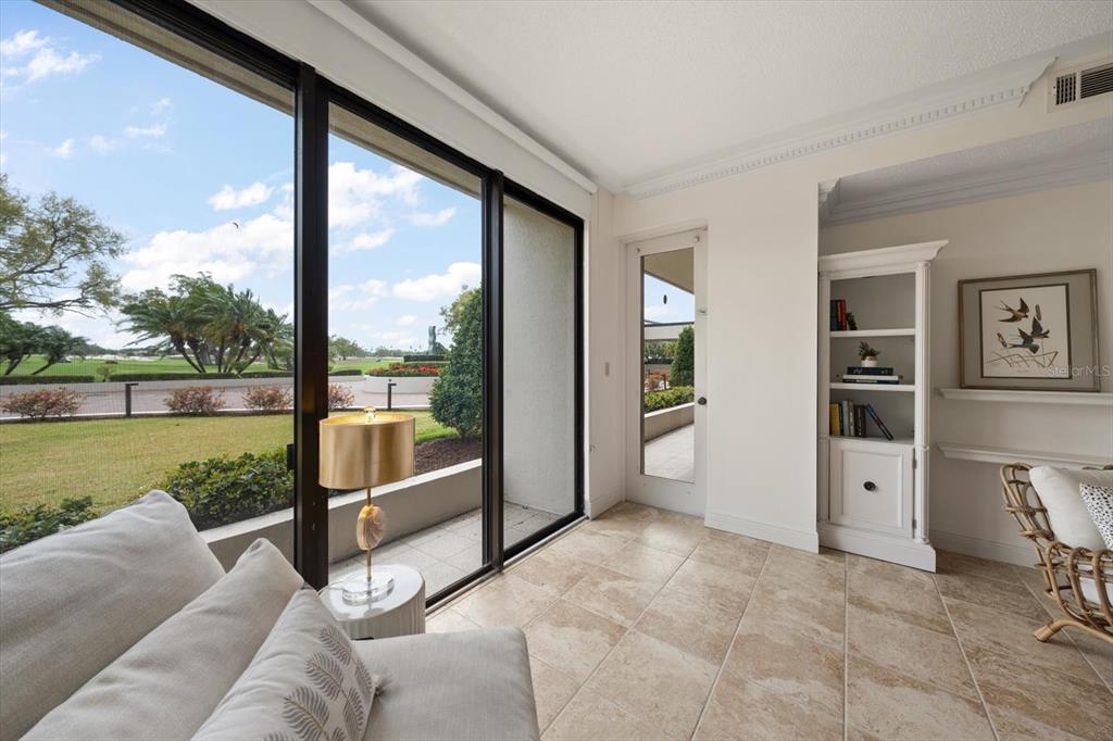 A sunroom with tile floors, a white bookshelf, and large windows overlooking a golf course — 4 BELLEVIEW BOULEVARD UNIT 106, BELLEAIR, FL