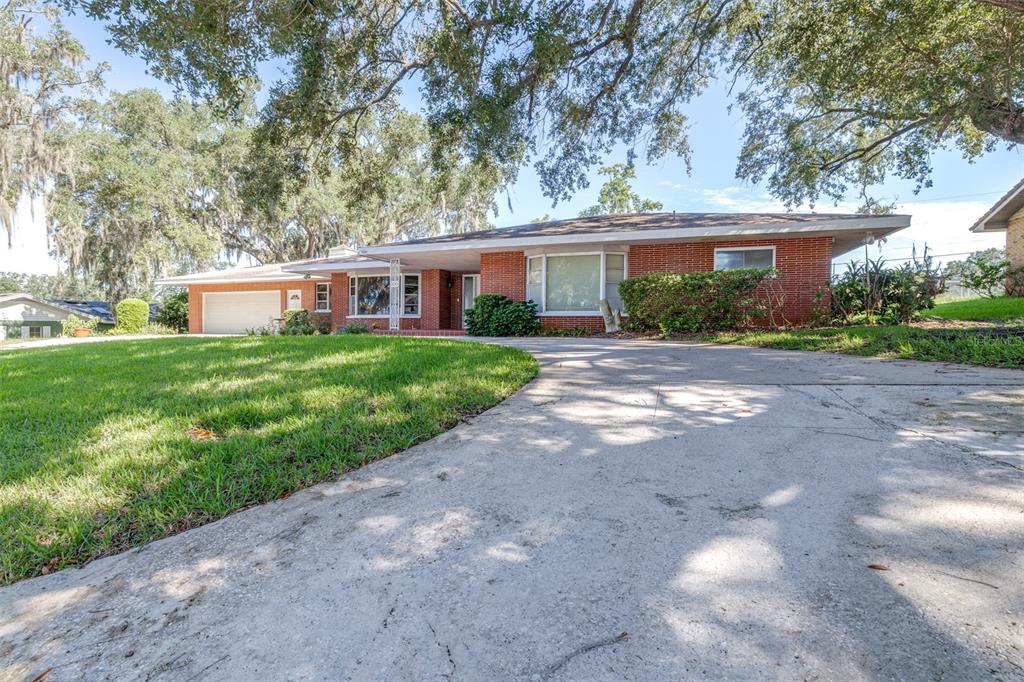 A single-story brick house with a concrete driveway and large oak trees in the yard — 300 CREST DRIVE, HAINES CITY, FL