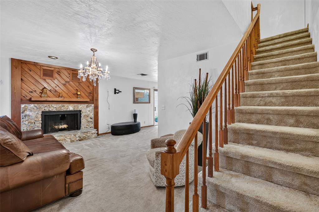 A living room features a stone fireplace, wood-paneled wall, chandelier, and a carpeted staircase — 2215 NE 45TH AVENUE UNIT 3, OCALA, FL