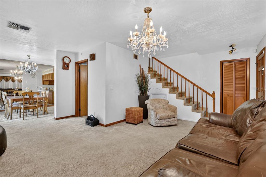A living room features a chandelier, carpeted floors, a staircase, and a leather sofa — 2215 NE 45TH AVENUE UNIT 3, OCALA, FL
