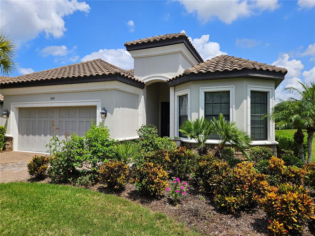 A single-story house with a tiled roof, beige stucco exterior, and a front-facing garage — 5668 CANTUCCI STREET, NOKOMIS, FL