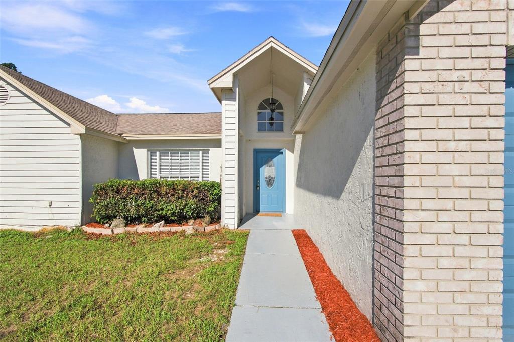 A light blue front door sits beneath a peaked entryway with a brick exterior wall — 4745 CANTERBURY DRIVE, LAND O LAKES, FL