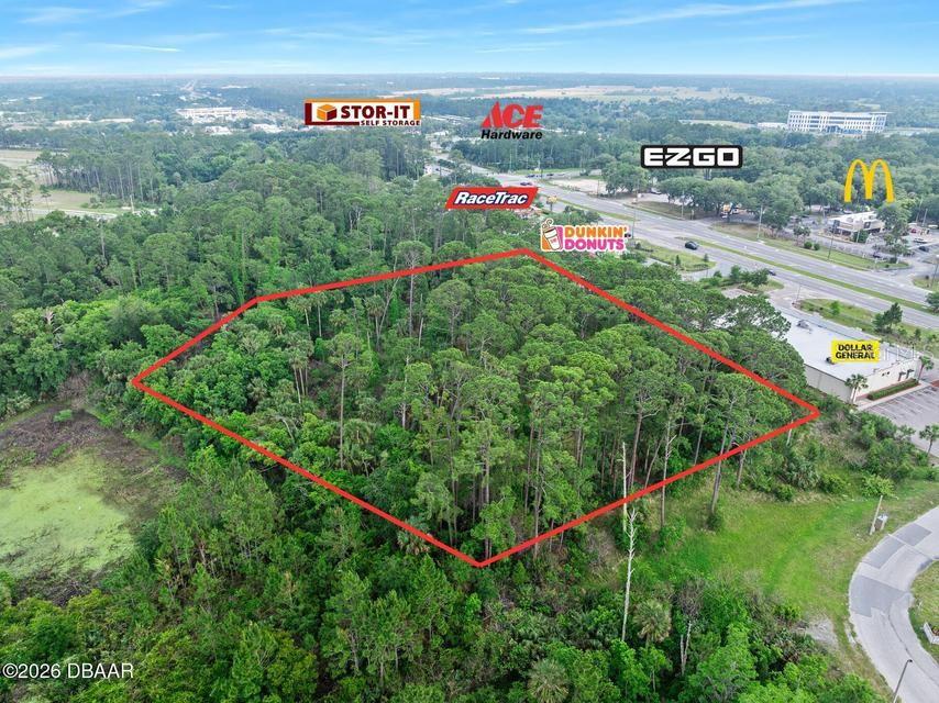 An aerial view shows a wooded, rectangular plot of land outlined in red near commercial businesses — 1128 BENTON STREET, ORMOND BEACH, FL