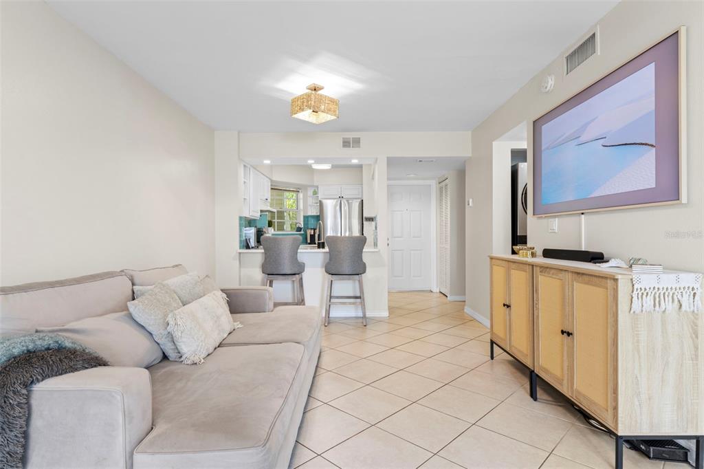 A living room with tile floors, a wall-mounted television, and an adjacent kitchen with stools — 6915 STONES THROW CIRCLE N UNIT 3104, ST PETERSBURG, FL