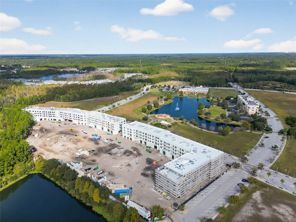 An aerial view shows a large multi-story building under construction near a lake and woods — 890 CENTRAL AVENUE UNIT E103, PALM COAST, FL