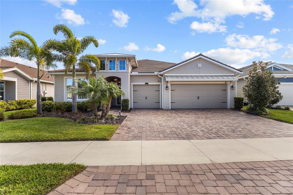 A single-story house with a beige exterior, a three-car garage, and a paver driveway — 5745 LONG SHORE LOOP, SARASOTA, FL
