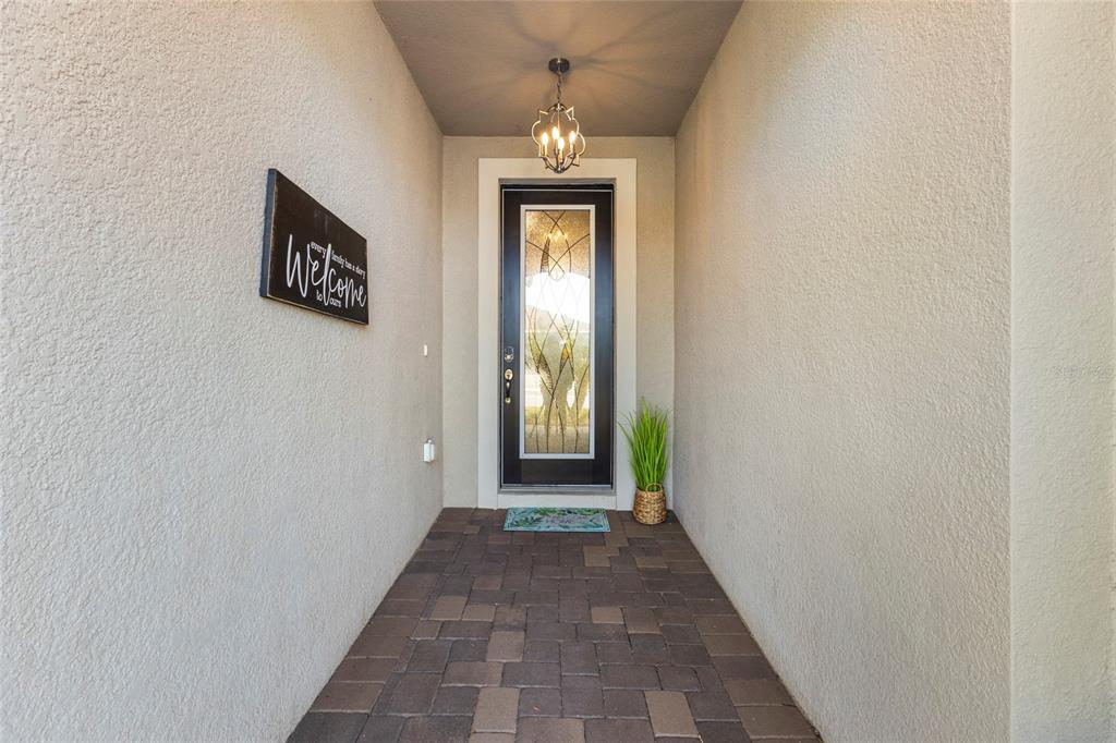 A covered entryway features a paver floor, a decorative glass front door, and a hanging light — 5745 LONG SHORE LOOP, SARASOTA, FL