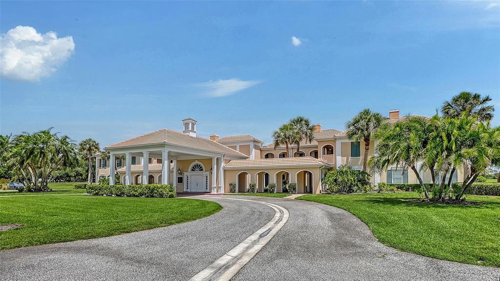 A large, multi-story estate with a porte-cochère, circular driveway, and palm trees under blue skies — 51 MACEWEN DRIVE UNIT 12, OSPREY, FL