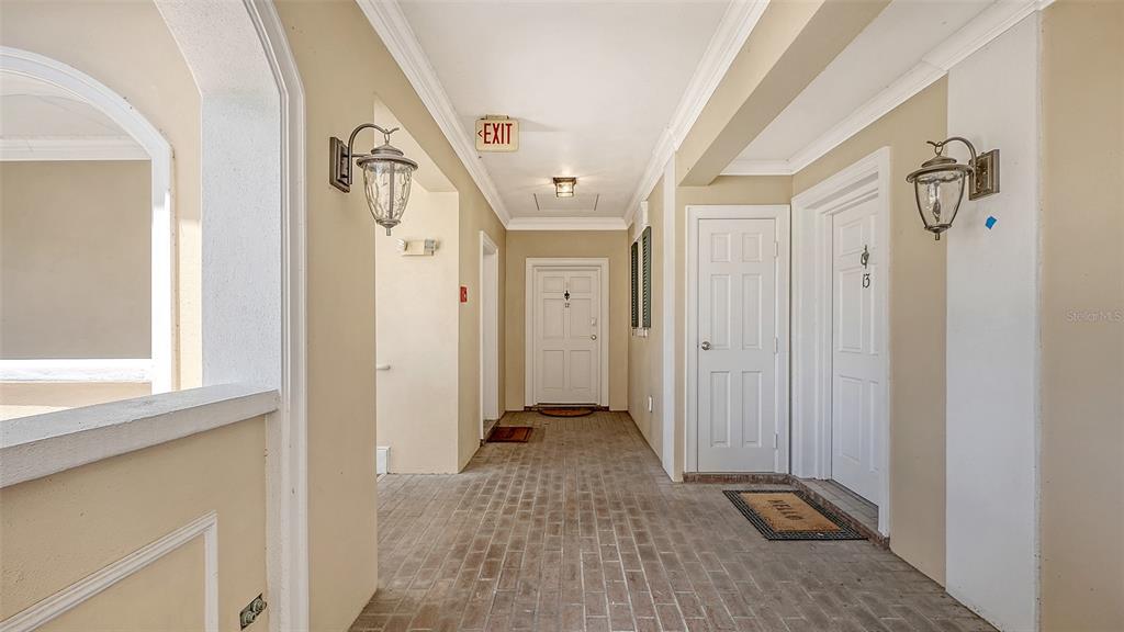 An outdoor apartment hallway with brick flooring, two white doors, and wall-mounted lanterns — 51 MACEWEN DRIVE UNIT 12, OSPREY, FL