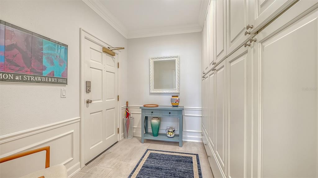 A bright entryway features white built-in cabinets, a blue console table, and a framed poster — 51 MACEWEN DRIVE UNIT 12, OSPREY, FL