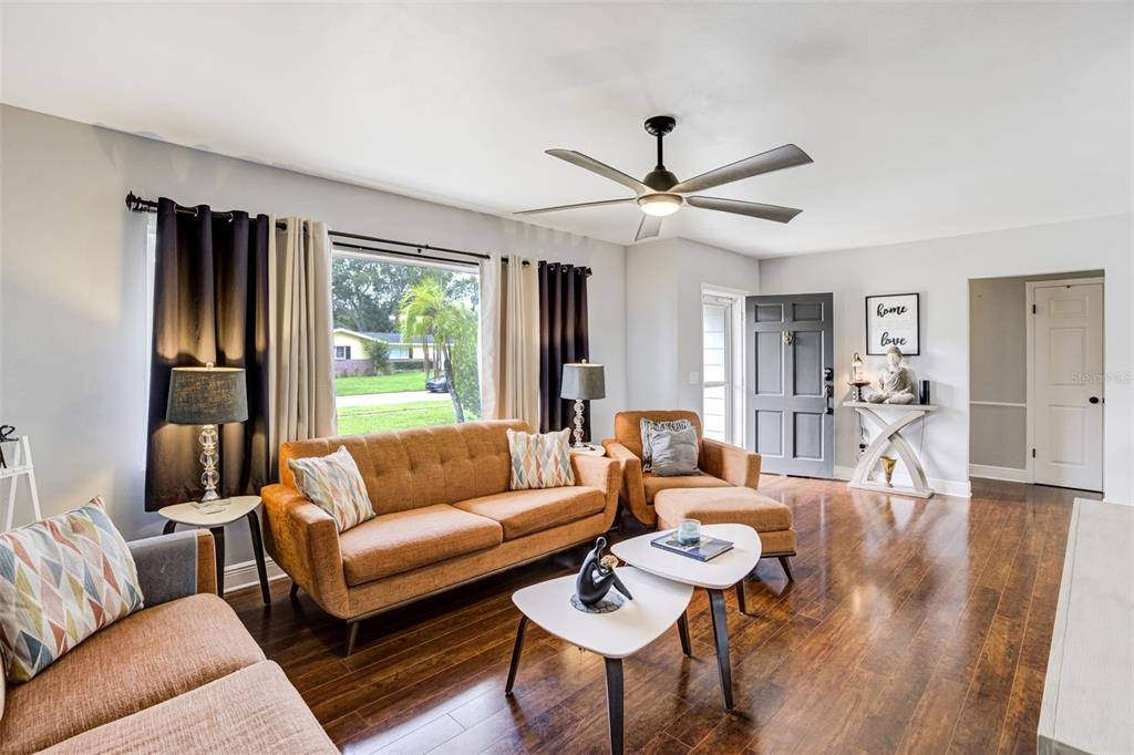 A living room features orange sofas, a television mounted above a fireplace console, and hardwood floors — 1636 LEISURE DRIVE, CLEARWATER, FL