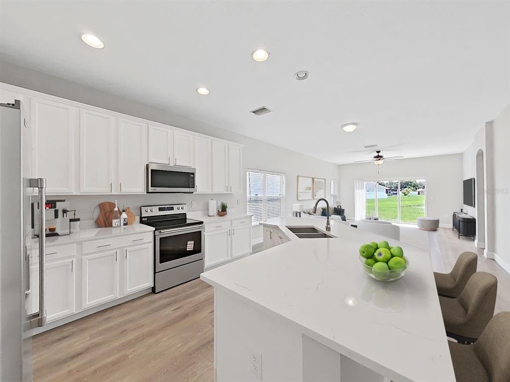 A modern kitchen features white cabinets, stainless steel appliances, and a large quartz-topped island — 11908 FERN BLOSSOM DRIVE, GIBSONTON, FL
