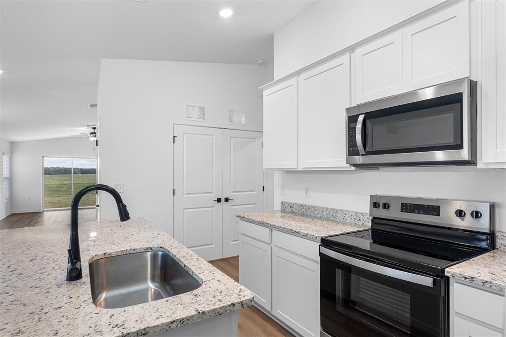 A kitchen with white cabinets, granite countertops, stainless steel appliances, and a kitchen island — 7142 CANOPY LANE, LAKELAND, FL