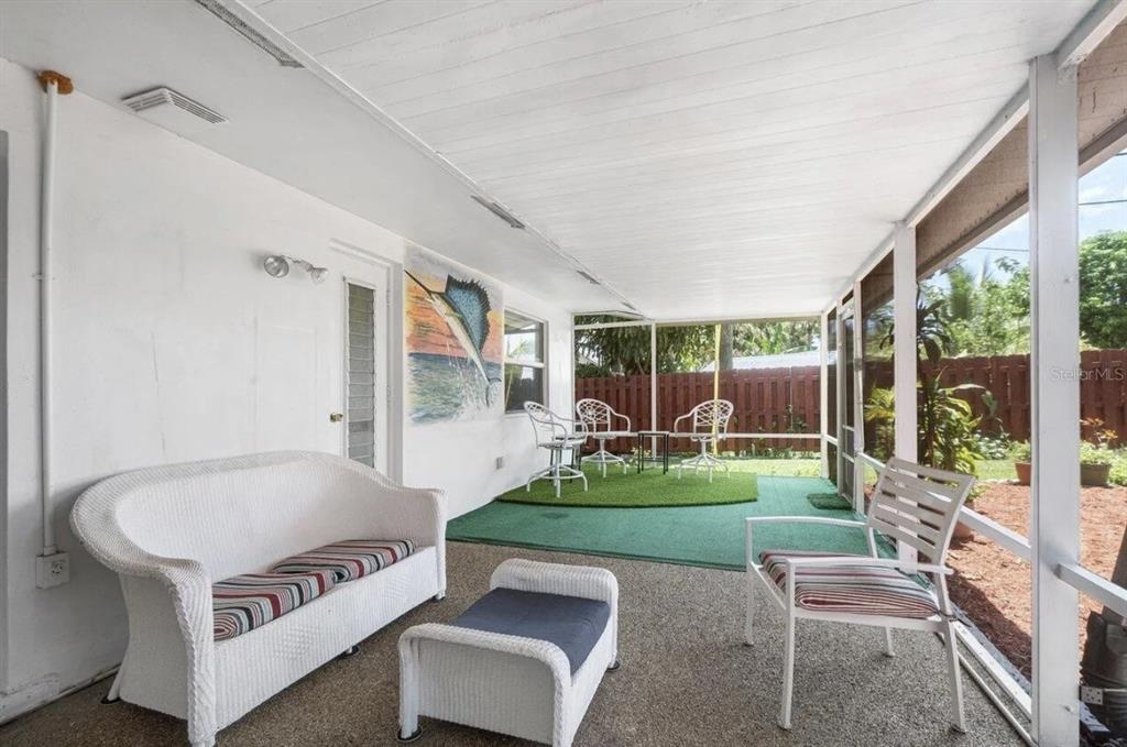 A screened-in porch features a white wicker sofa, matching chairs, and a green turf area — 717 LINDELL BOULEVARD, DELRAY BEACH, FL