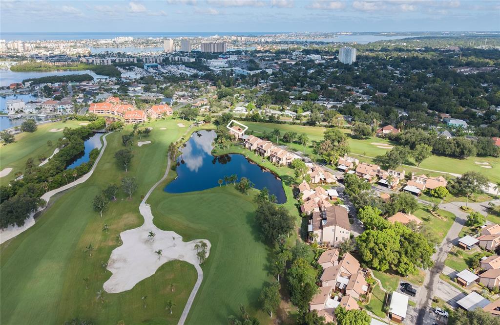 An exterior view of a multi-story tan building with a tile roof near a pond — 1328 PELICAN CREEK CROSSING UNIT D, ST PETERSBURG, FL