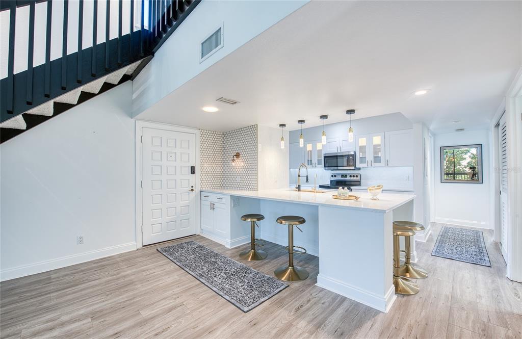 A kitchen with a breakfast bar and a living area featuring a mirrored wall — 1328 PELICAN CREEK CROSSING UNIT D, ST PETERSBURG, FL