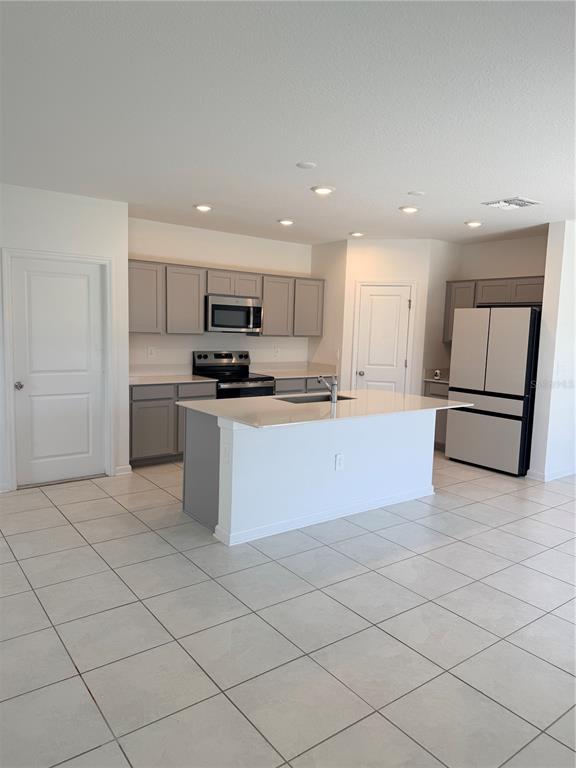 A kitchen features gray cabinets, stainless steel appliances, a white island, and light tile flooring — 2847 BIG SUR ROAD, DAVENPORT, FL