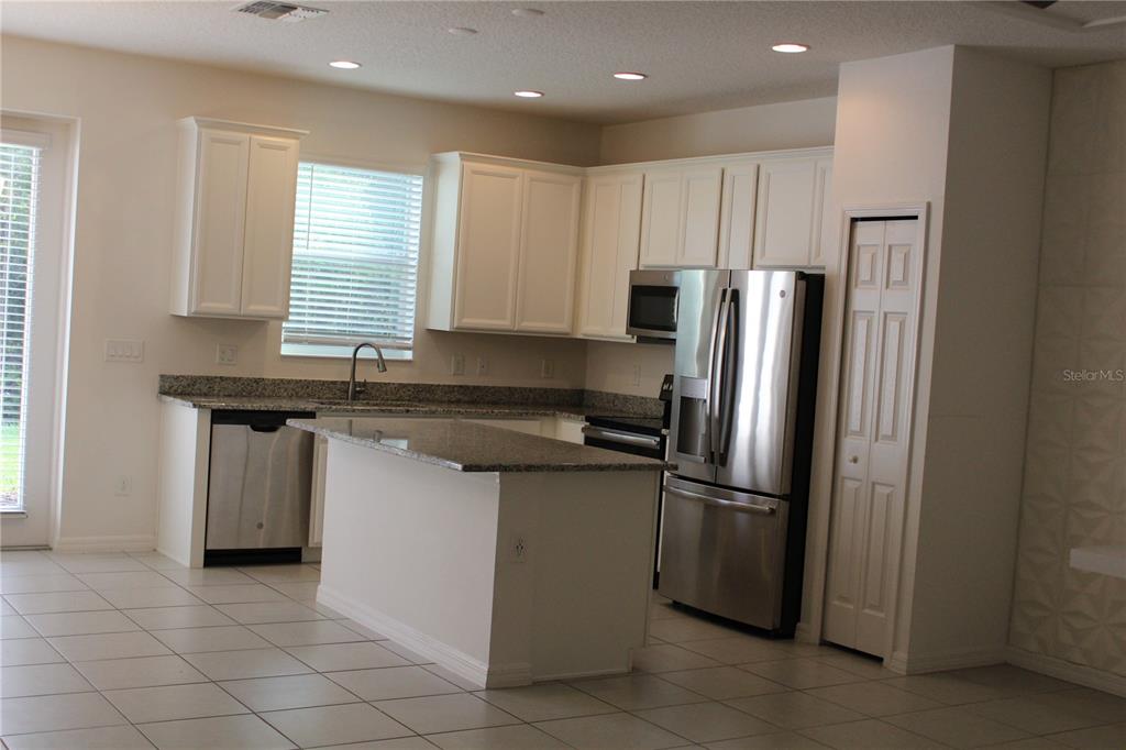A kitchen features white cabinets, granite countertops, stainless steel appliances, and light-colored tile flooring — 2193 SEDGE GRASS WAY, ORLANDO, FL