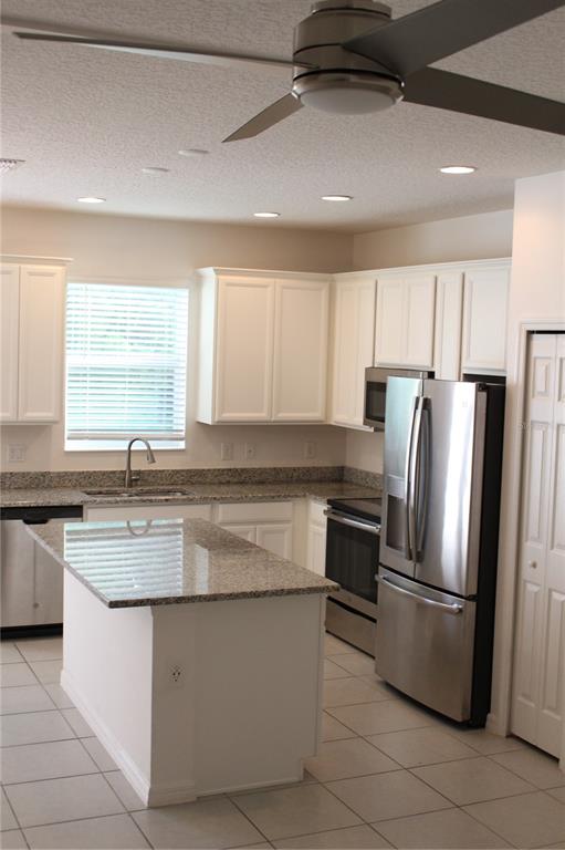 A kitchen features white cabinets, granite countertops, a center island, and stainless steel appliances — 2193 SEDGE GRASS WAY, ORLANDO, FL