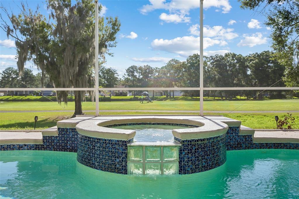 A pool and spa with blue tile accents overlook a green golf course — 15611 SHOAL CREEK PLACE, ODESSA, FL