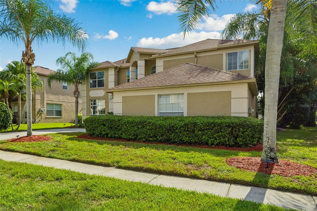 A two-story tan stucco townhouse with a hip roof and a manicured hedge in front — 15611 SHOAL CREEK PLACE, ODESSA, FL