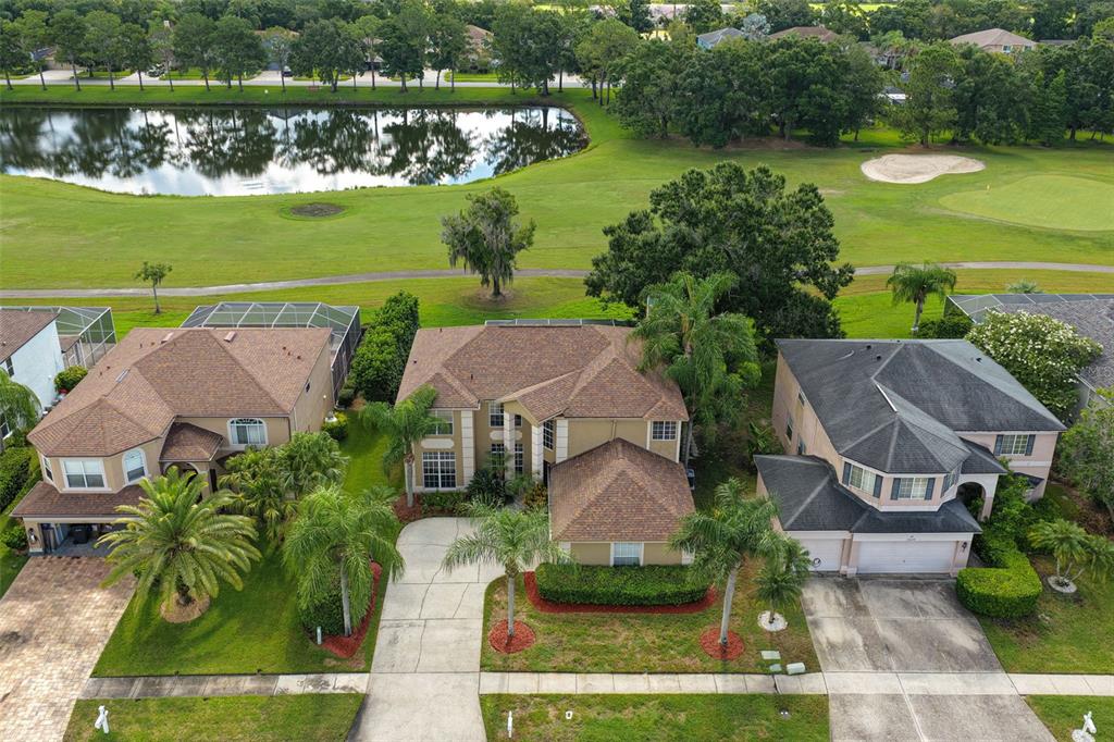 An aerial view shows three suburban houses with brown roofs situated along a golf course — 15611 SHOAL CREEK PLACE, ODESSA, FL