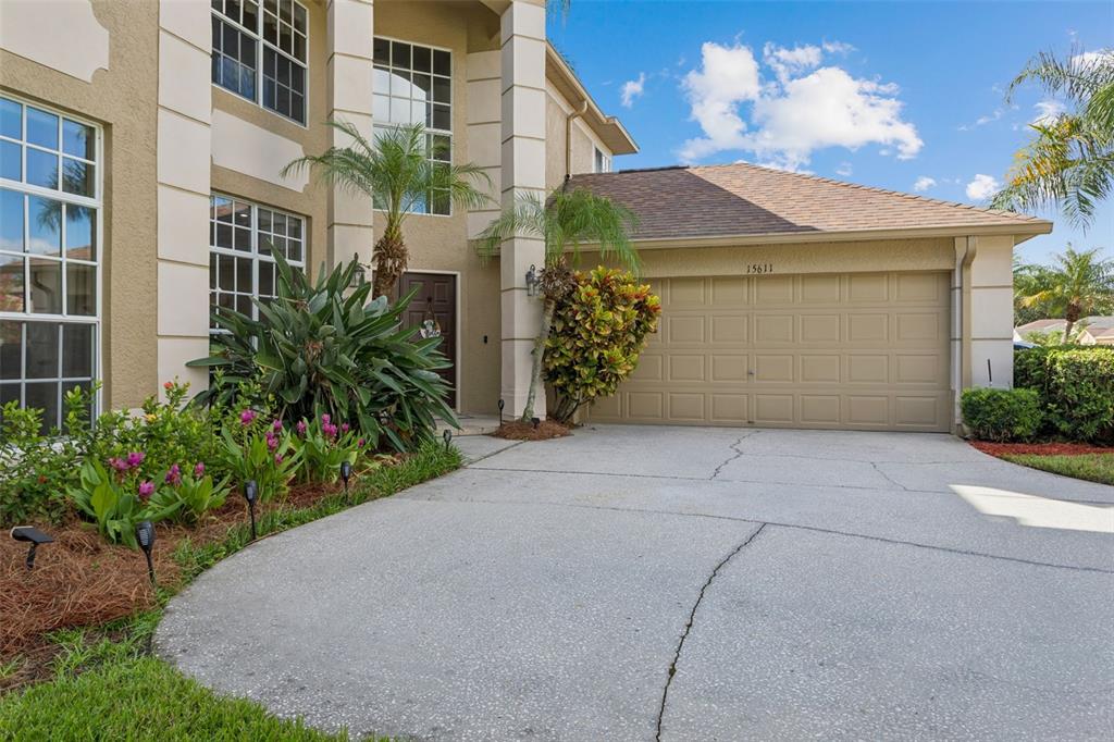 A two-story house exterior features a beige stucco facade, a garage, and a concrete driveway — 15611 SHOAL CREEK PLACE, ODESSA, FL