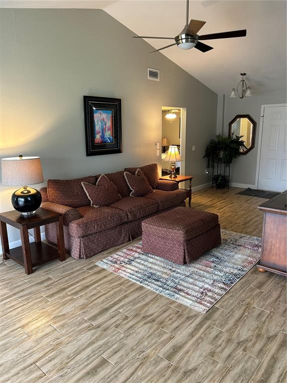 A living room features a patterned sofa, matching ottoman, wood-look tile flooring, and vaulted ceilings — 13236 MOLITOR COURT, HUDSON, FL