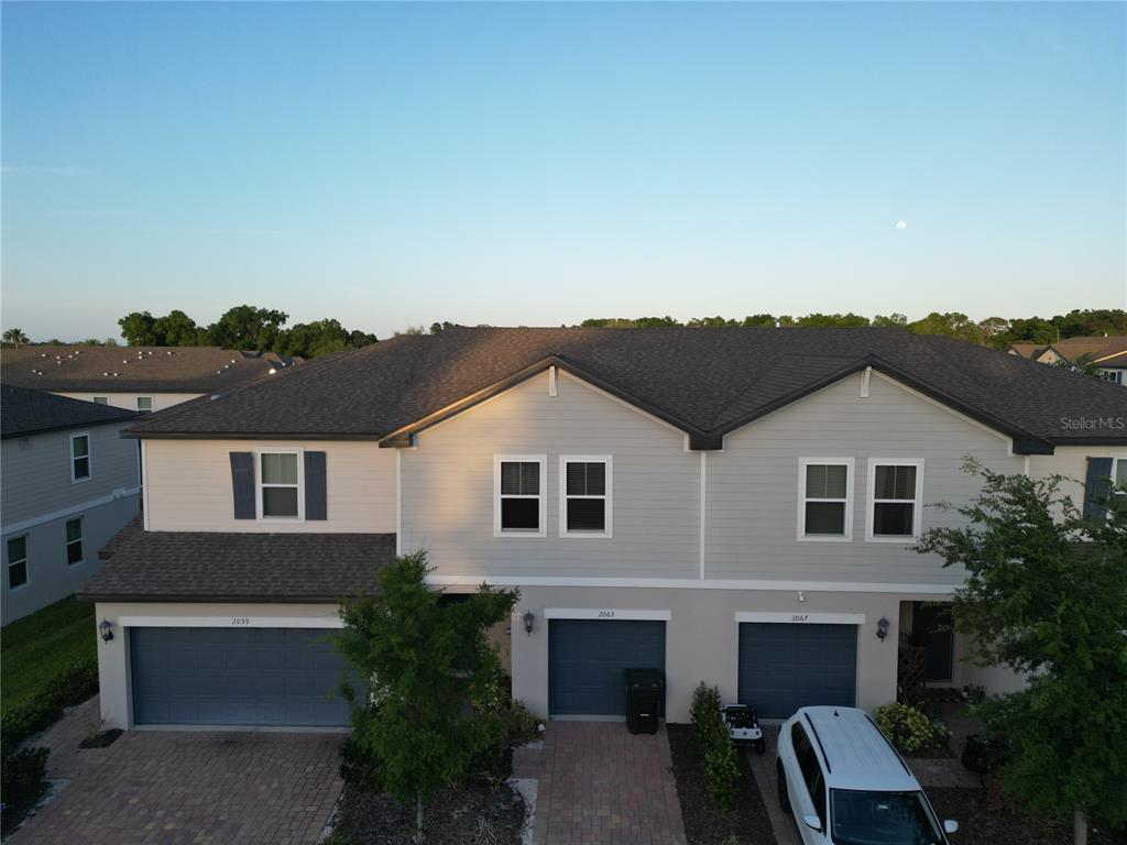An aerial view shows the front exterior of three attached townhomes with garages and driveways — 2063 HAREBELL LANE, OCOEE, FL
