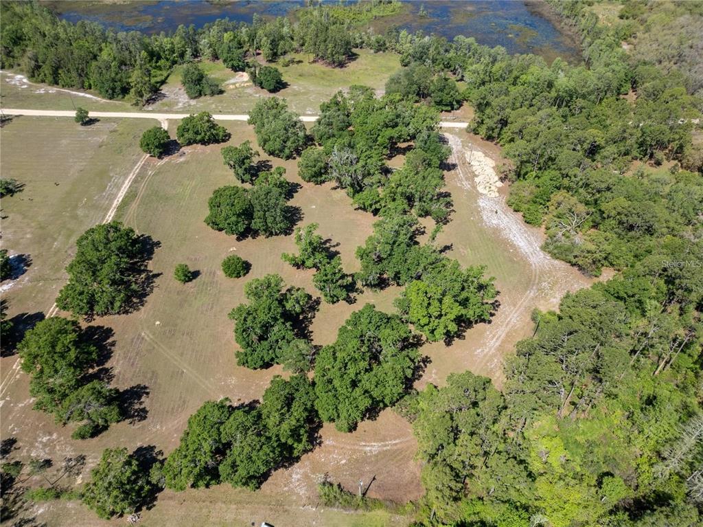 An aerial view shows a grassy, tree-dotted lot with a dirt driveway and nearby wetlands — DR BAKER ROAD, GROVELAND, FL