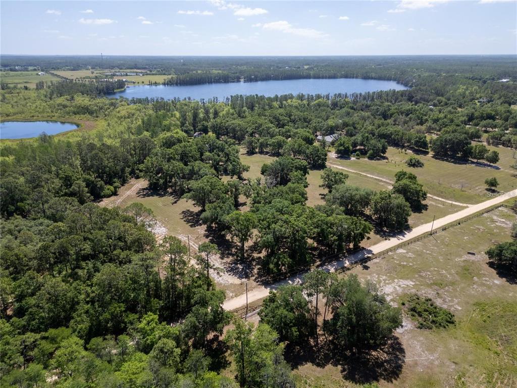 An aerial view shows a large, wooded lot with a dirt road and a lake nearby — DR BAKER ROAD, GROVELAND, FL
