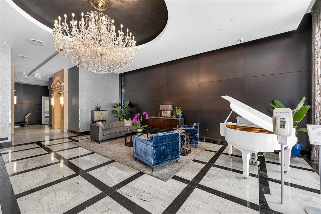 A luxurious lobby features a crystal chandelier, white grand piano, and dark wood paneled walls — 100 S EOLA DRIVE UNIT 1005, ORLANDO, FL